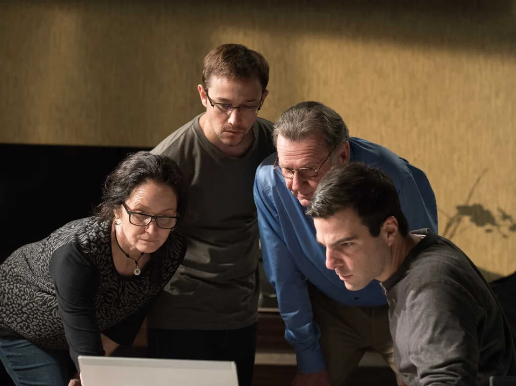 Four people—three men and one woman—lean in closely around a laptop, concentrating on the screen in a warmly lit room with a beige wall, as if engrossed in discussing thrilling Cyber Movies. | IFVOD-TV.com